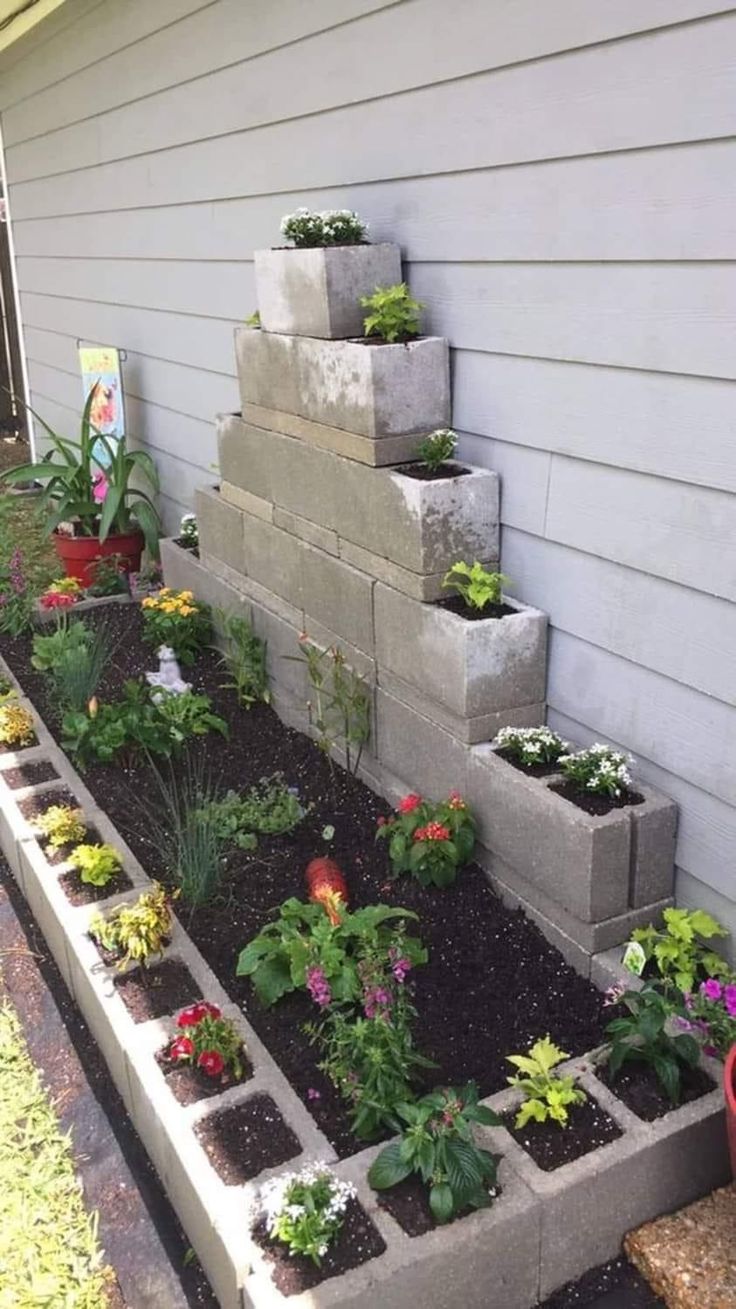 an outdoor garden with concrete blocks and flowers in the center, along side a house