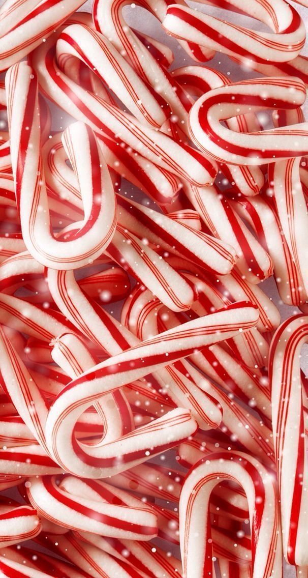 red and white candy canes are piled up in the air with snow falling on them