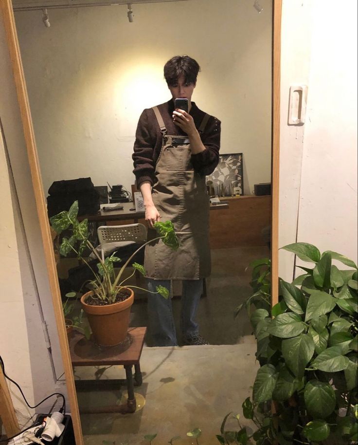 a man standing in front of a mirror holding a cell phone next to a potted plant