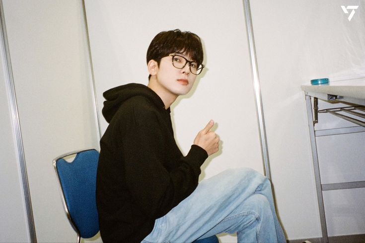 a young man sitting on top of a blue chair in front of a white wall