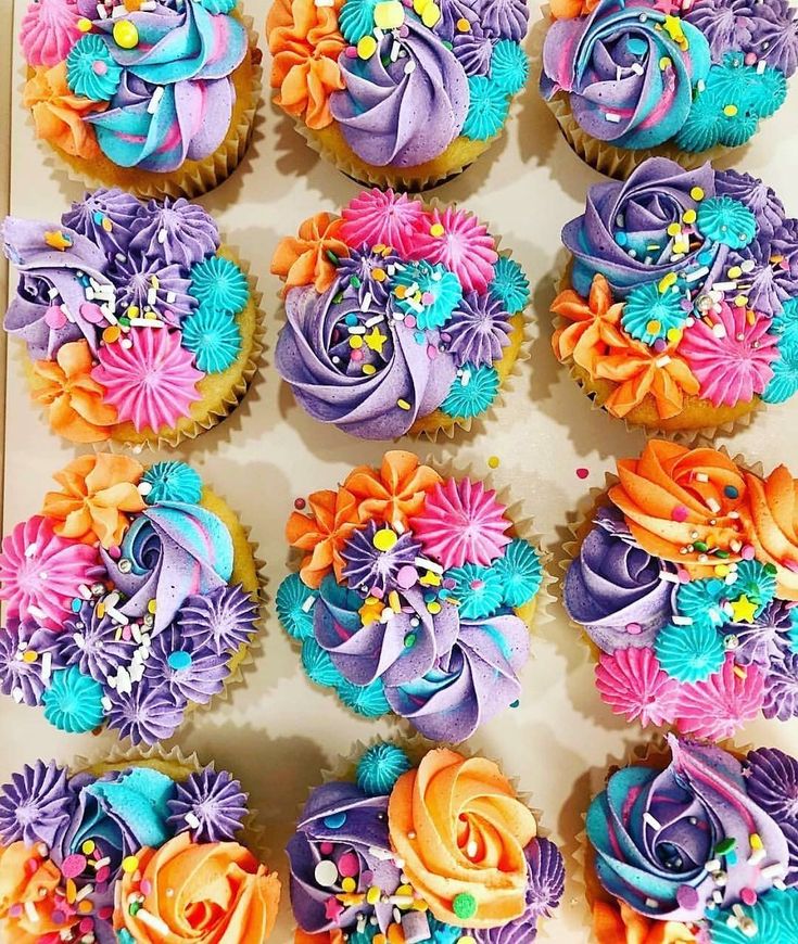 there are many cupcakes decorated with flowers on the top one is purple, orange and blue