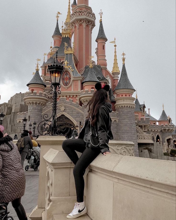 a woman sitting on the edge of a stone wall in front of a large castle