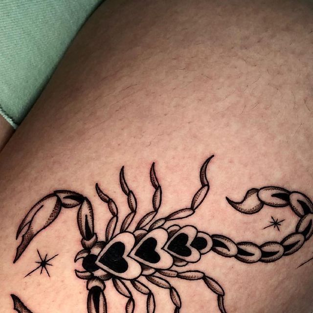 a black and white scorpion tattoo on the thigh, with hearts in it's claws