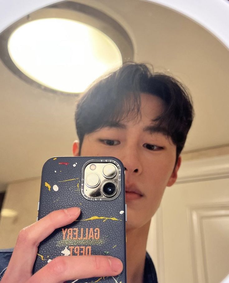 a young man taking a selfie with his cell phone in front of the mirror