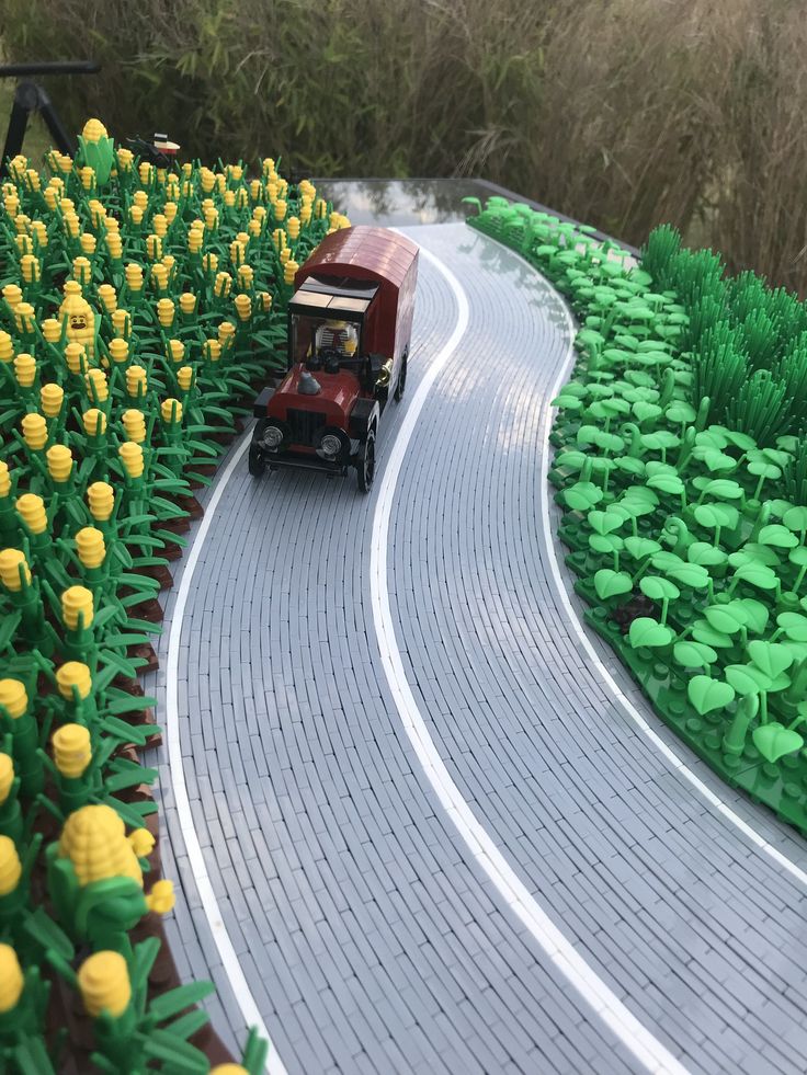 a toy truck driving down a road surrounded by flowers