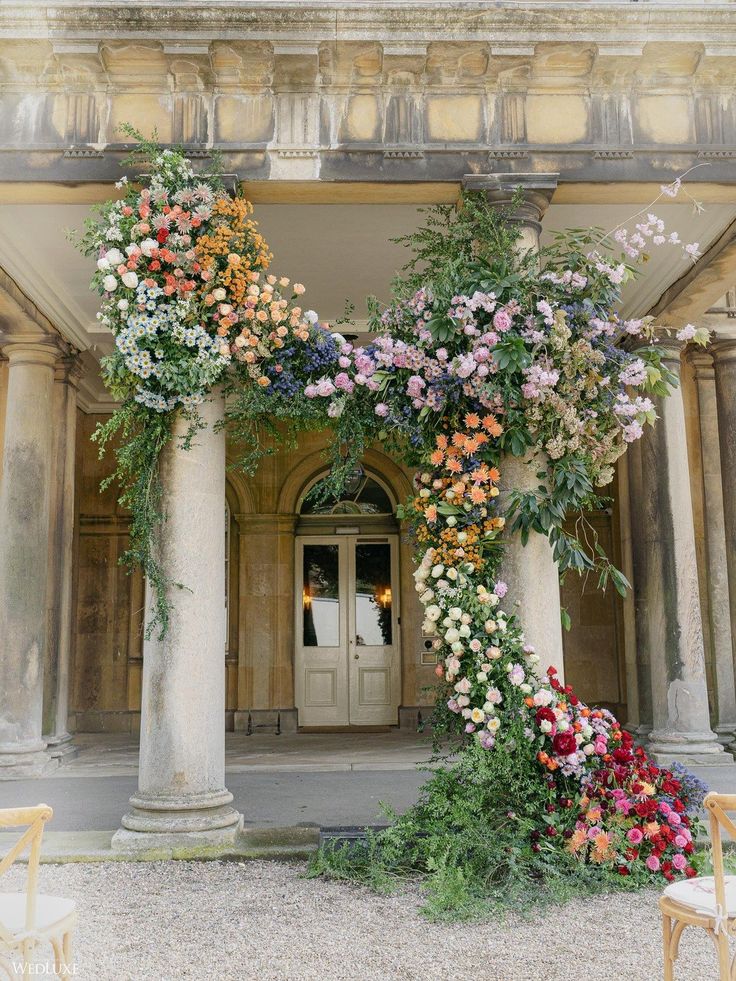 an arch covered with flowers and greenery in front of a door way to a building