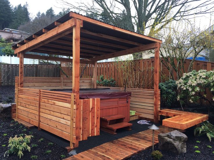 an outdoor hot tub in the middle of a garden with wooden benches and plants around it