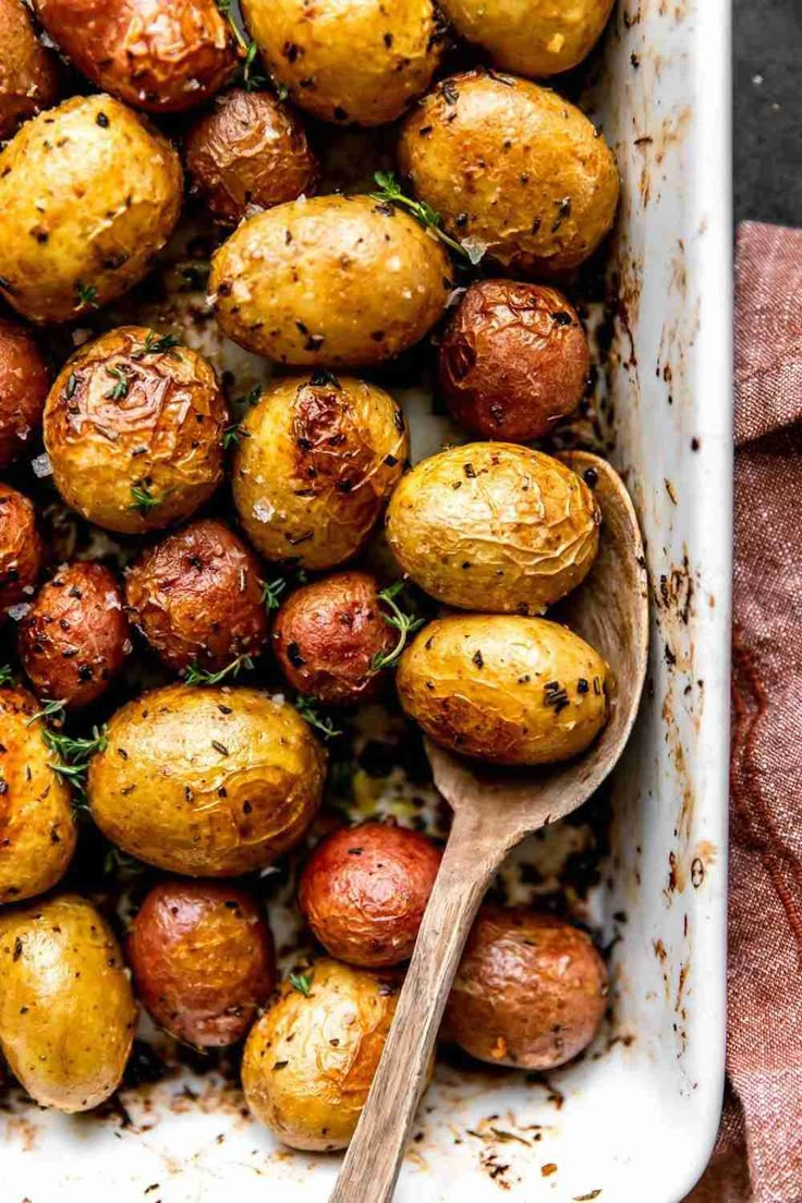 a casserole dish filled with roasted potatoes and garnished with fresh herbs