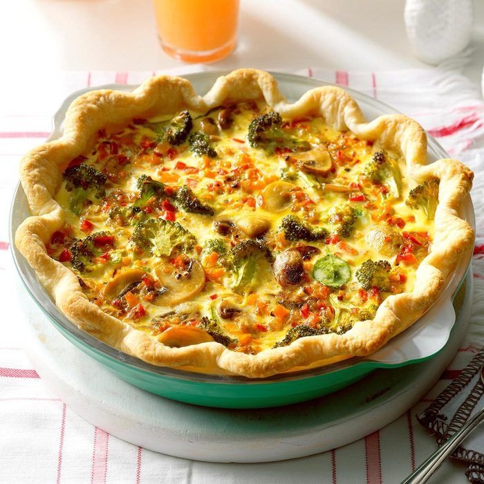 a quiche with broccoli, peppers and cheese on a plate next to a glass of orange juice