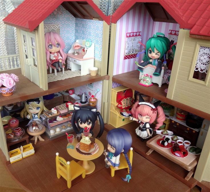 two dolls are standing in front of a doll house with other toys on the table