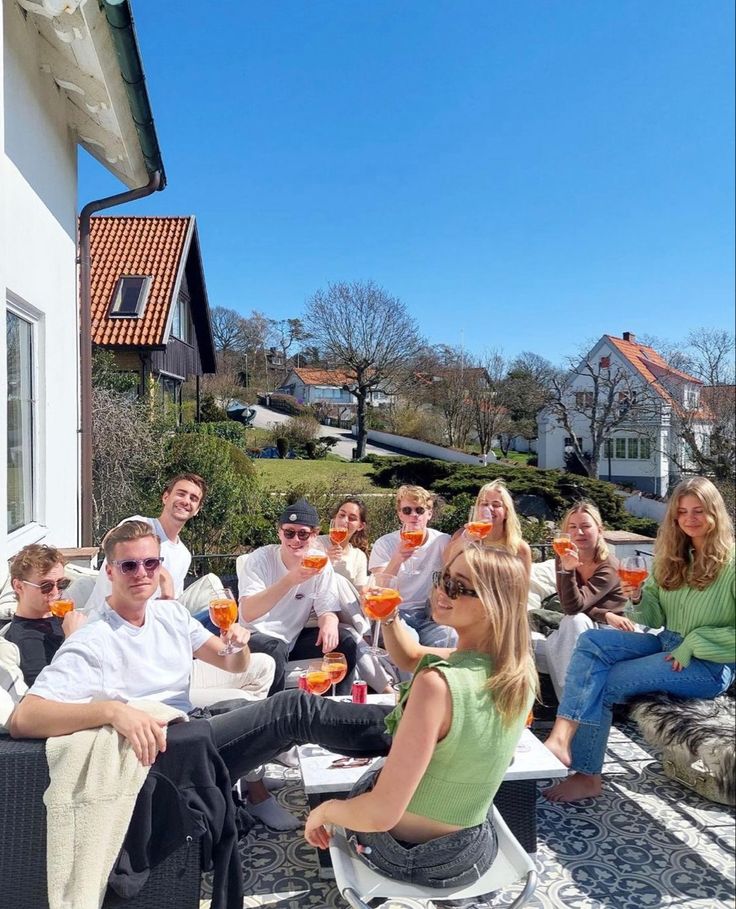 a group of people sitting on top of a patio next to each other holding drinks