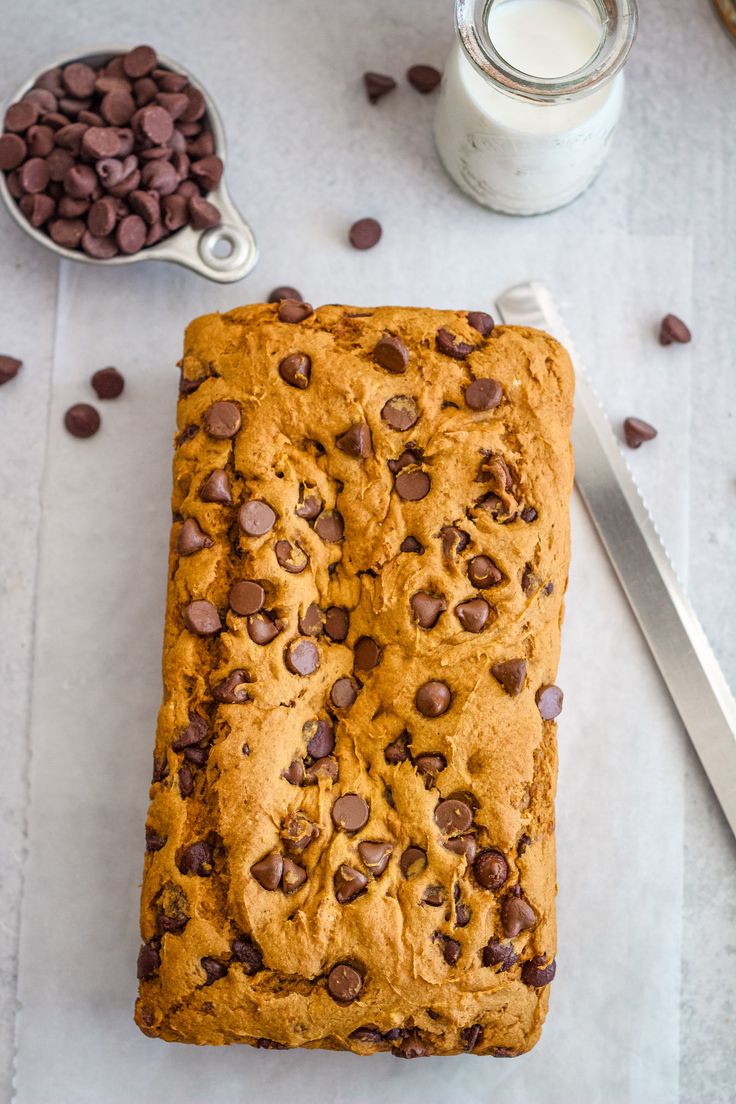 a loaf of chocolate chip bread sitting on top of a cutting board next to a glass of milk