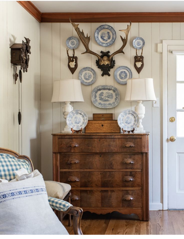 a wooden dresser topped with blue and white plates next to a deer head mounted on the wall