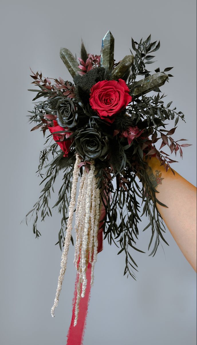 a bouquet of flowers is being held up by someone's hand with red and green foliage