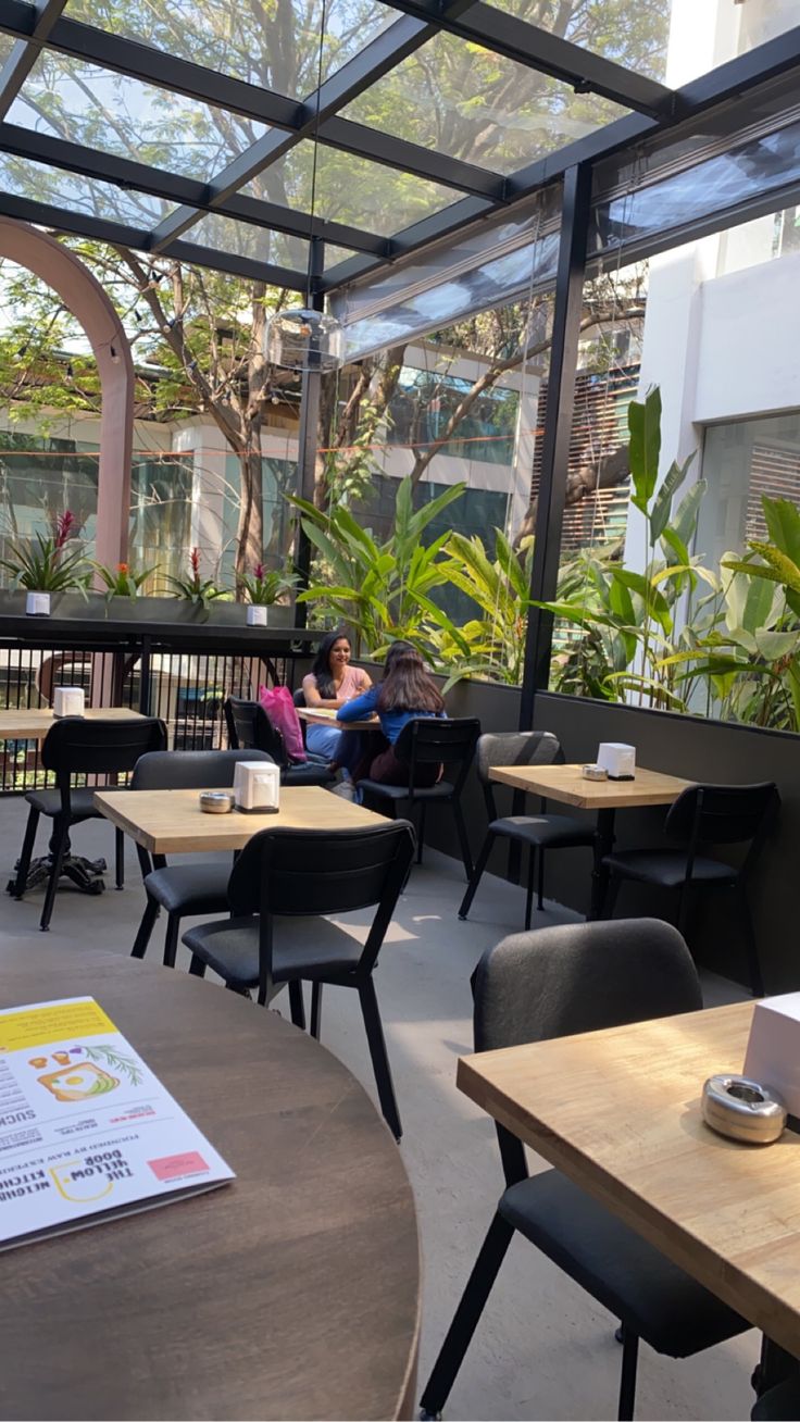 people are sitting at tables in an enclosed area with plants on either side of them