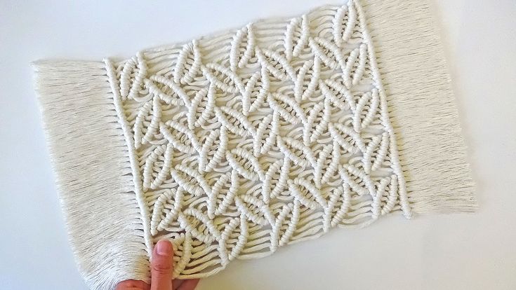 someone is holding up a piece of white yarn on top of a tablecloth with an intricate design