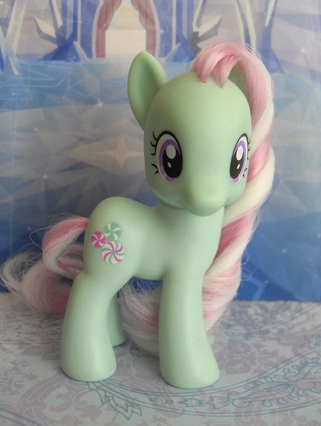 a green pony with pink manes sitting on top of a white table next to a blue wall