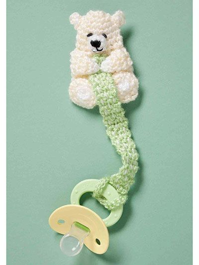 a crocheted teddy bear hanging from a hook on a green wall next to a pacifier