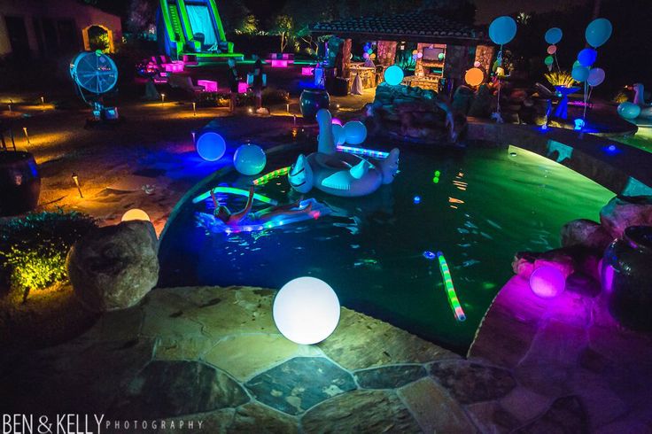 an outdoor pool at night with colorful lights and decorations on the water features inflatable balls