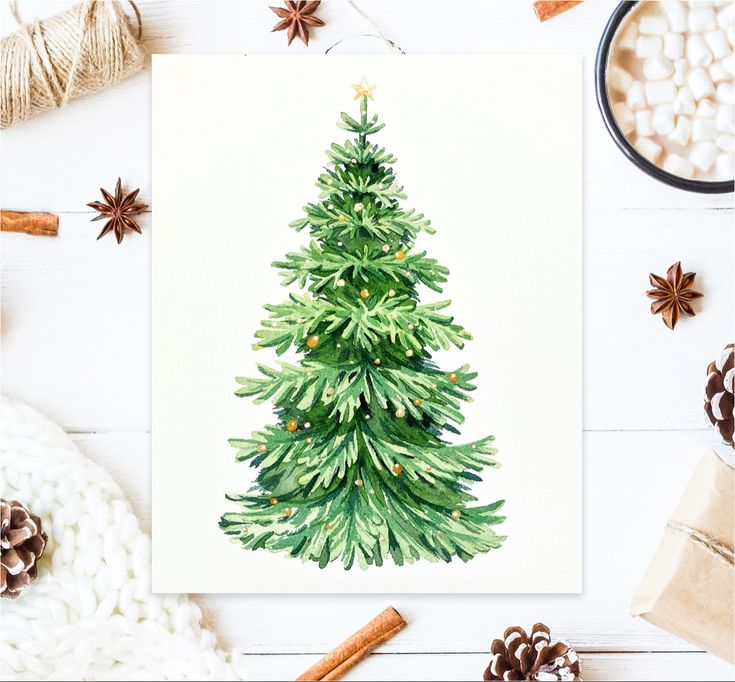 a watercolor christmas tree card on a white table with cinnamons and other holiday decorations