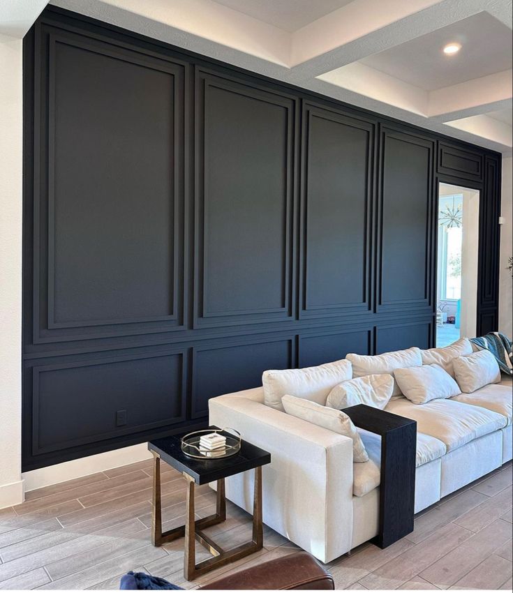 a living room with black paneled walls and white couches in front of a fireplace