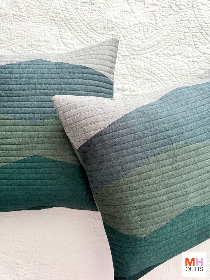 two pillows sitting on top of each other in front of a white bed with green and blue stripes