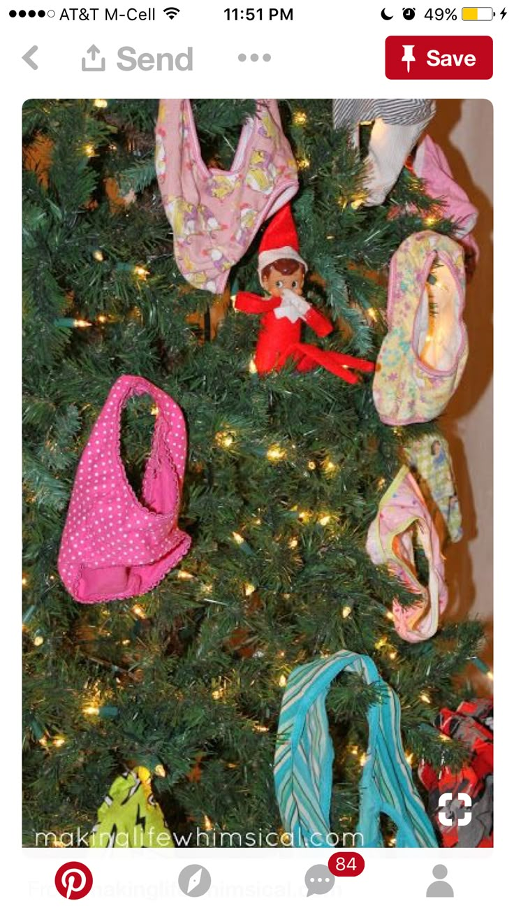 an elf is sitting in front of a christmas tree with many handbags on it