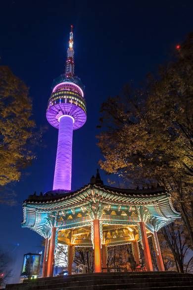 a tall tower lit up at night in the background with trees and lights around it