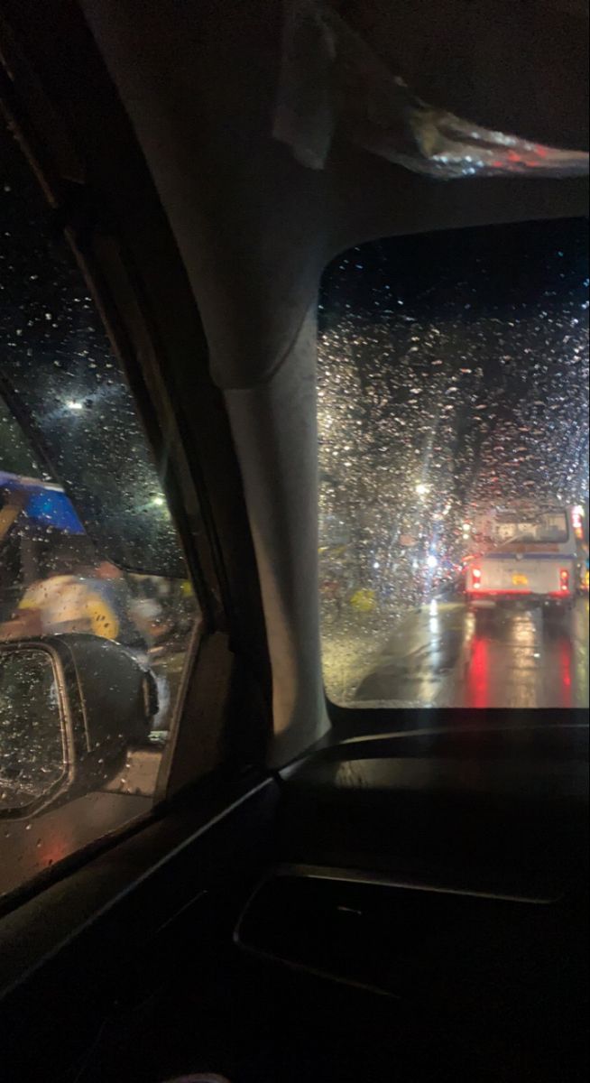 rain is falling on the windshield of a car as it drives down a street at night