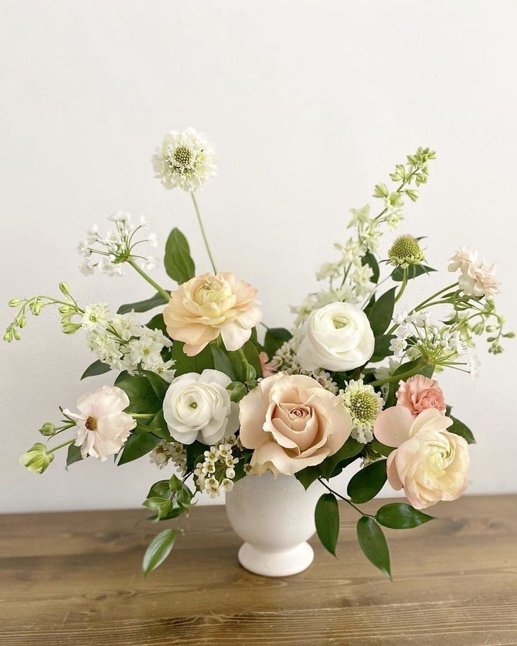 a white vase filled with flowers on top of a wooden table