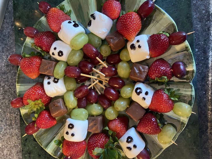 a plate with fruit and marshmallows shaped like panda faces on sticks in the center