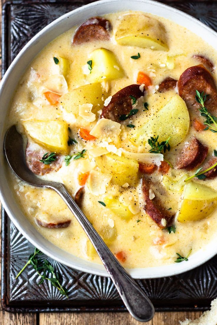 a white bowl filled with potatoes and sausage next to a spoon on top of a wooden table