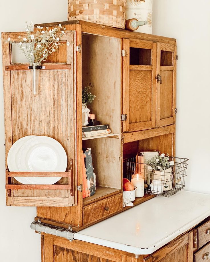 an old wooden cabinet with plates and flowers on it's shelf next to a white counter top