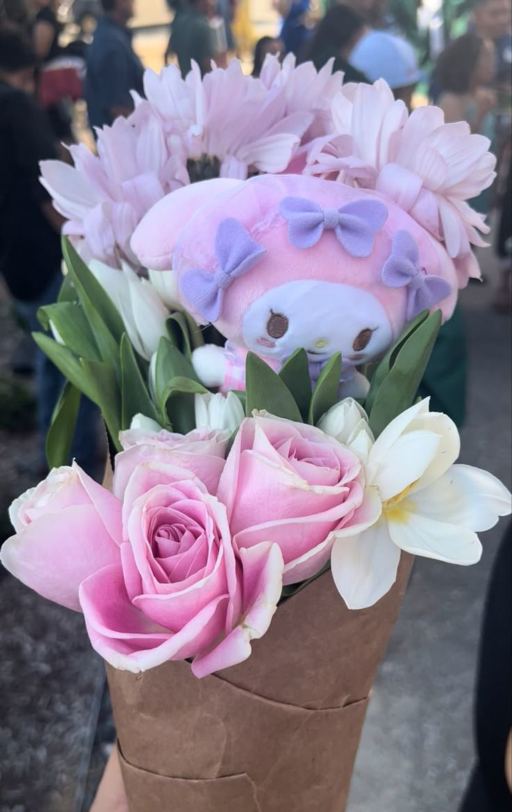 a teddy bear sitting on top of a brown vase filled with pink and white flowers