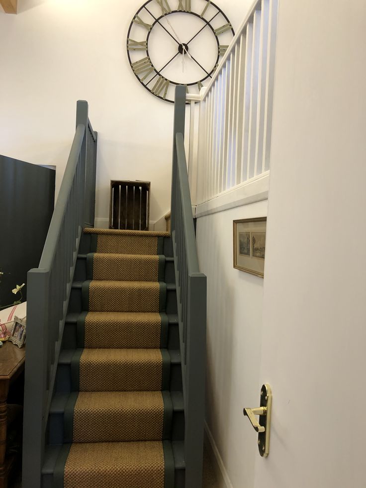 a clock on the wall next to stairs in a hallway with carpeted steps and wooden handrails