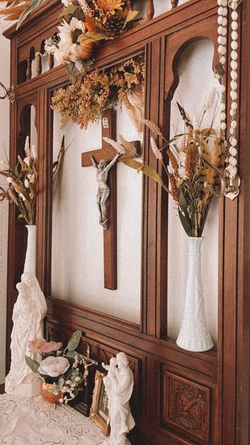 a cross and flowers are on the wall in front of a table with vases