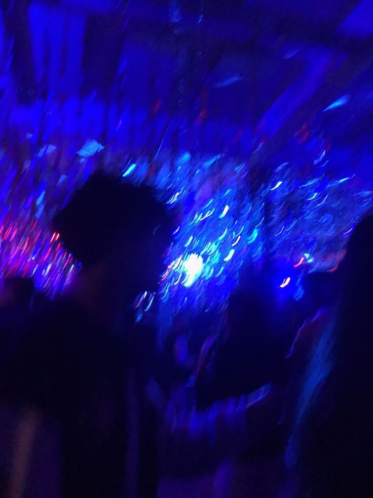 some people are standing around in a room with blue lights on the ceiling and one person is holding a cell phone