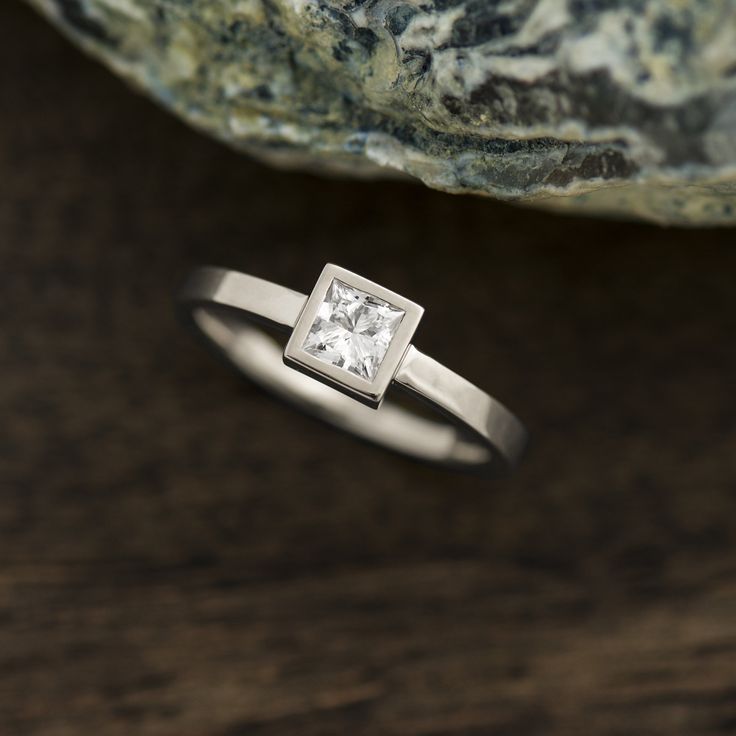 a gold ring with a princess cut diamond on it sitting next to a large rock