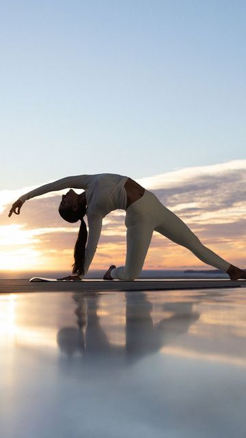 a woman doing yoga on the beach at sunset