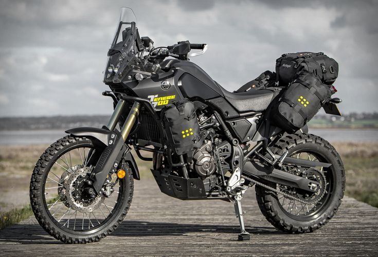 a black motorcycle parked on top of a wooden platform next to a body of water