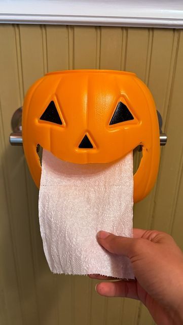 a person holding a roll of toilet paper in front of a pumpkin shaped tissue dispenser