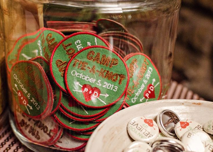 a glass jar filled with lots of green and red badges next to a pile of coins