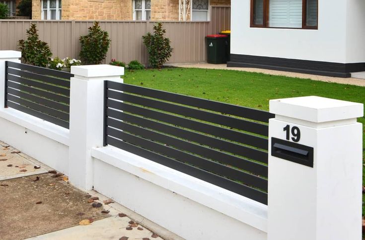 a white fence with black slats in front of a house and grass area next to it