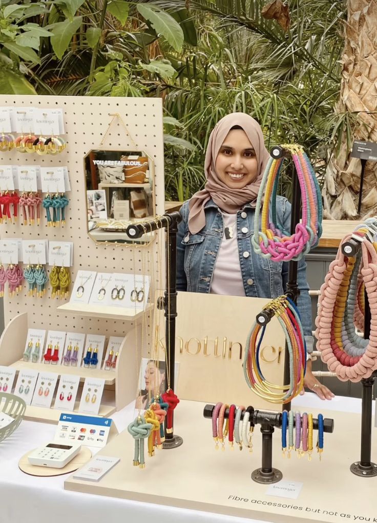 a woman is standing behind a table with bracelets on it and other items in front of her