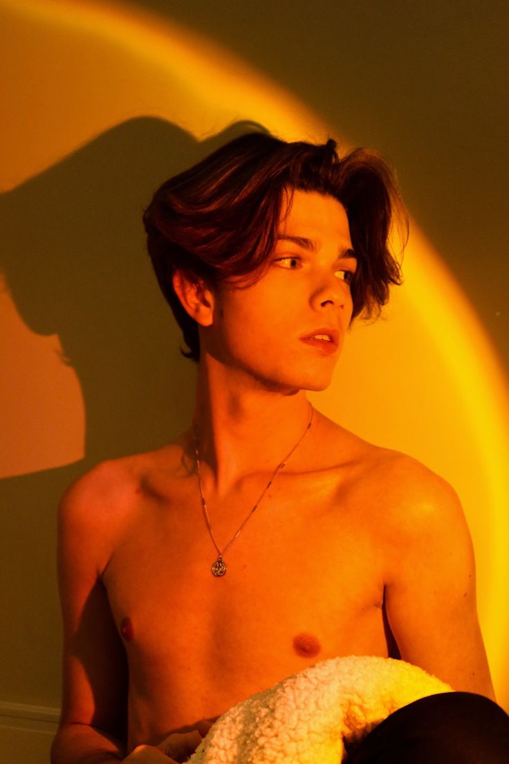 a shirtless young man sitting in front of a yellow circle with his shadow on the wall