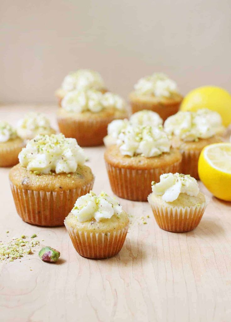 cupcakes with white frosting and lemon slices on a wooden table next to a lemon slice