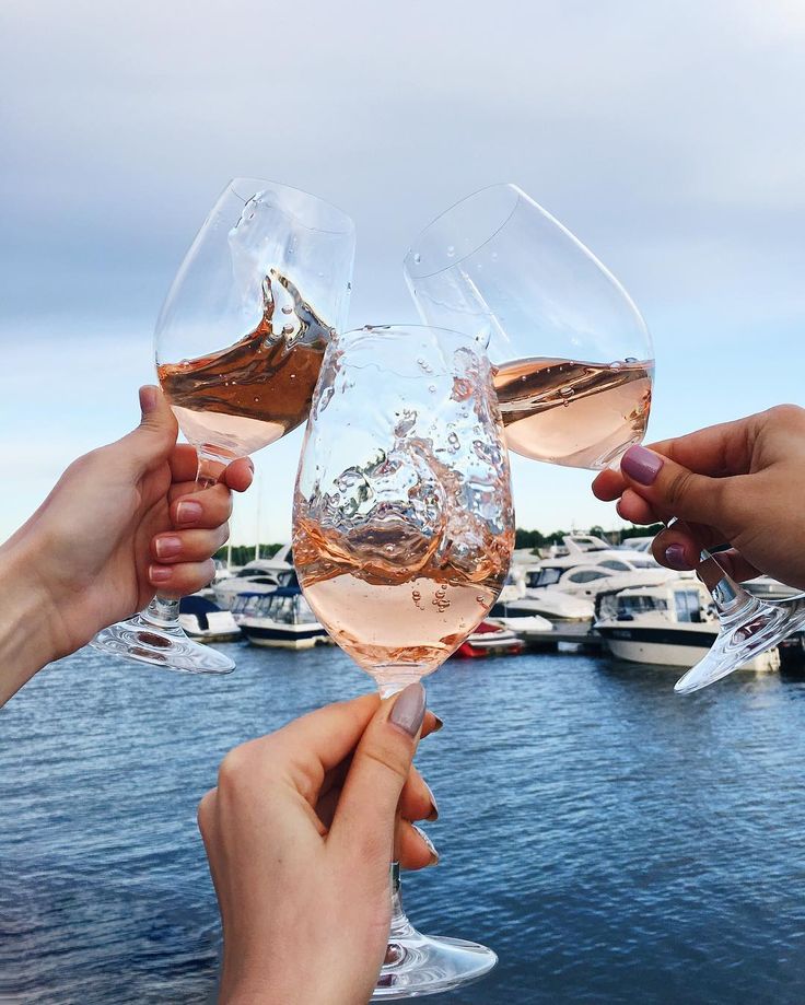 two people toasting with wine glasses in front of a body of water and boats