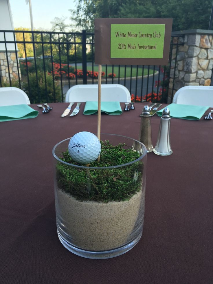 a golf ball sitting in a glass cup filled with sand and grass on top of a table