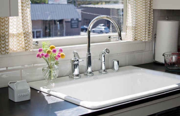 a kitchen sink sitting under a window next to a counter top with flowers in it