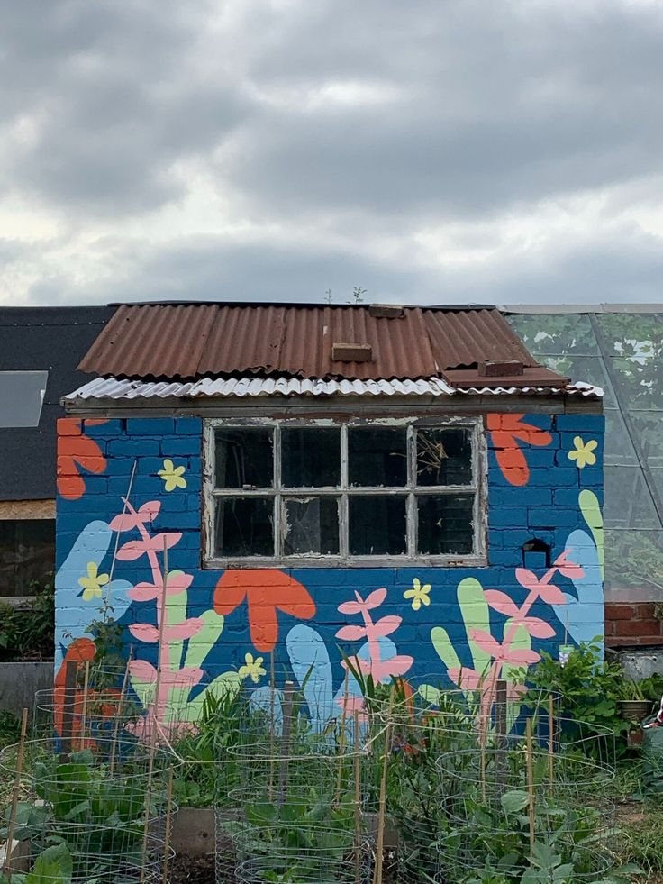 a blue building with flowers painted on it's side next to a garden area